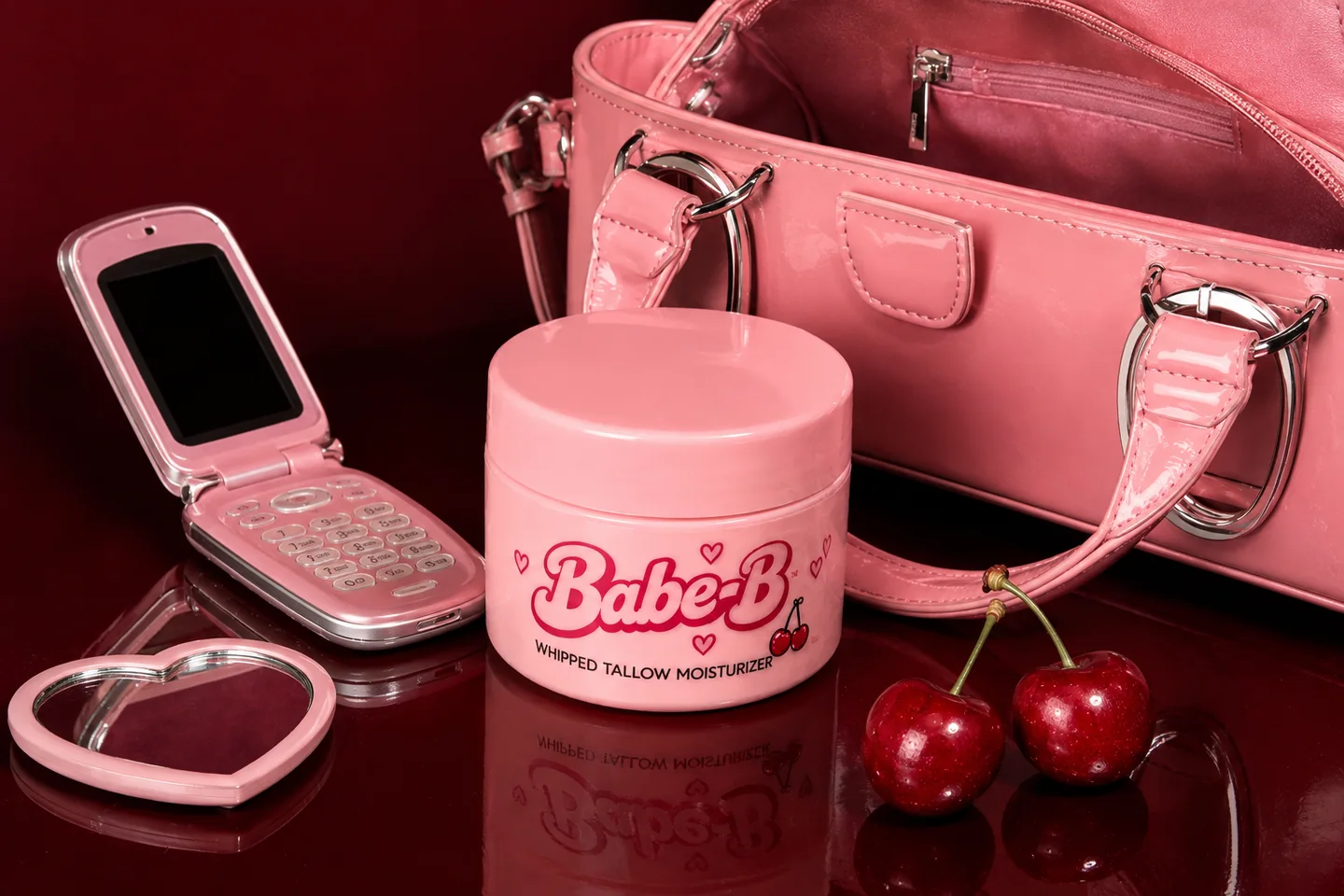 Babe-B pink bag, flip phone, heart mirror and jar on a cherry-red tabletop