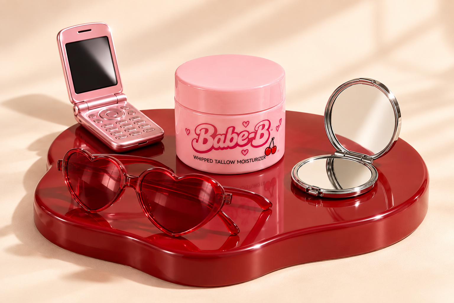Pink flip phone, heart sunglasses, chrome compact and Babe-B jar on a red display