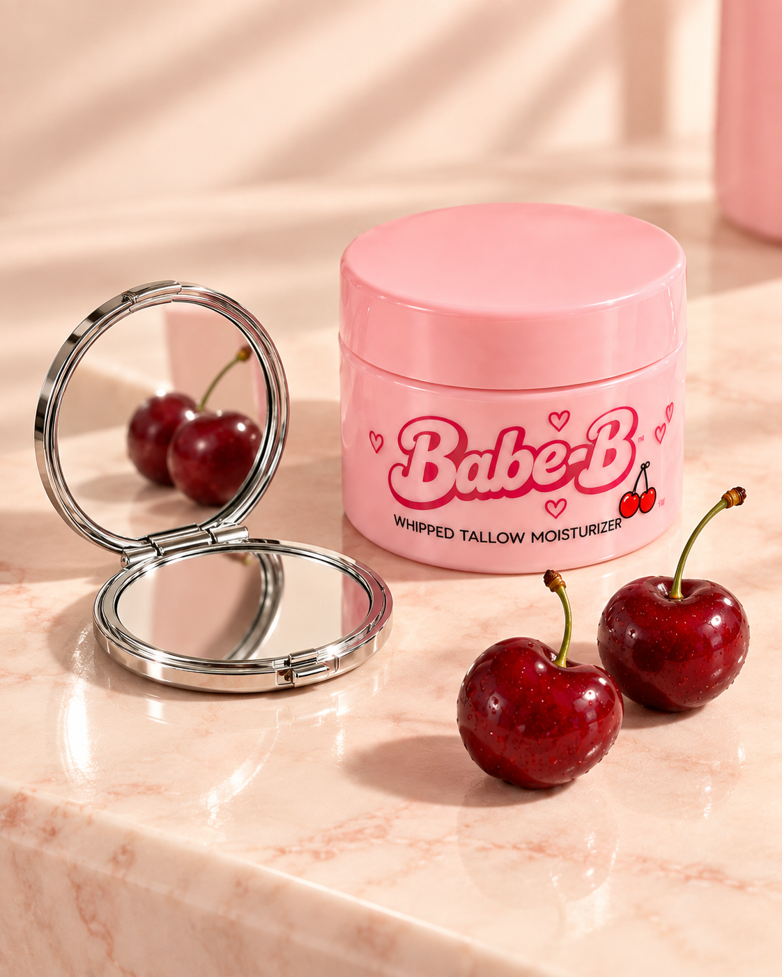 Open chrome compact reflecting cherries beside a pink Babe-B jar